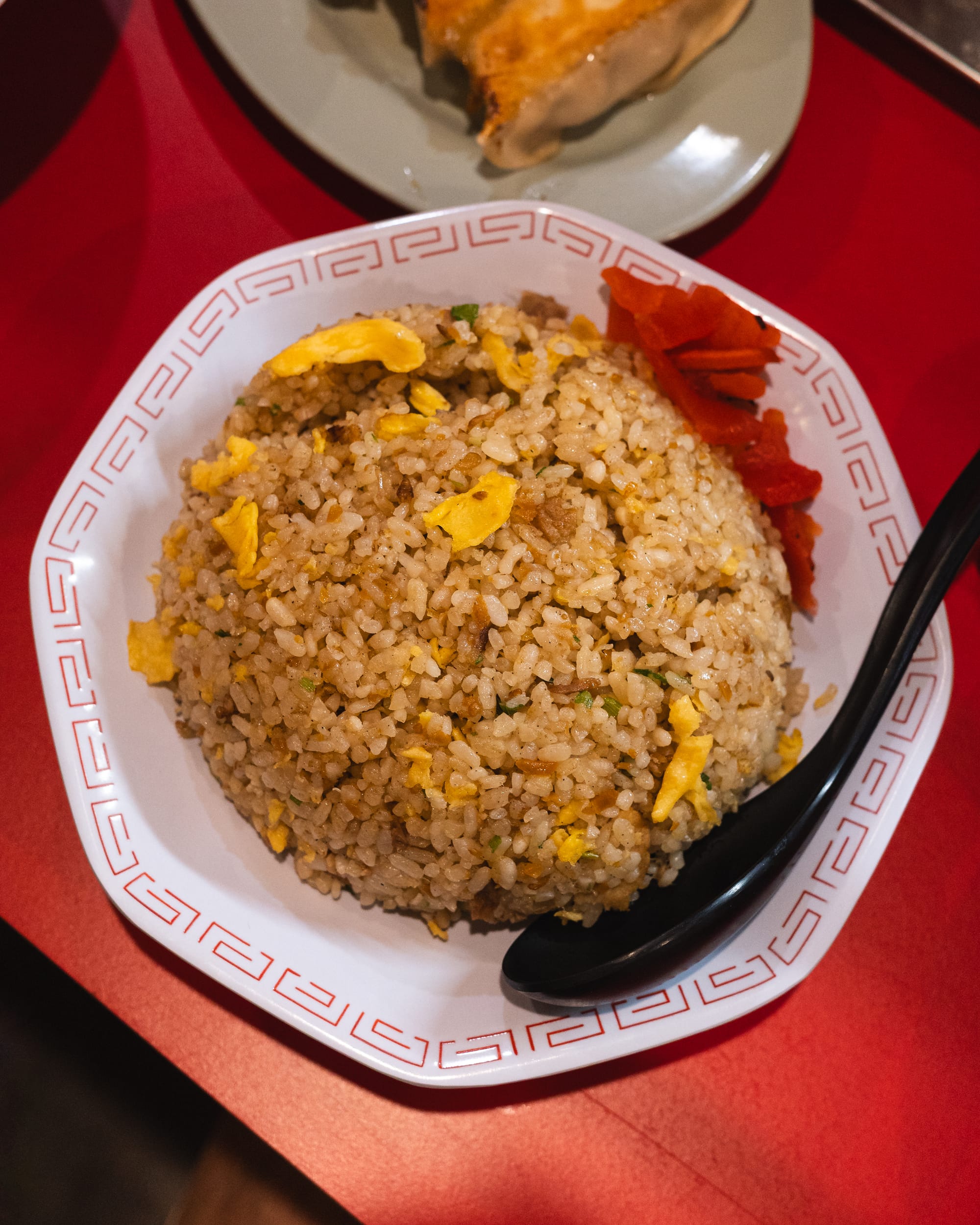 A bowl of fried rice with egg, served in a white and red patterned bowl on a red table.