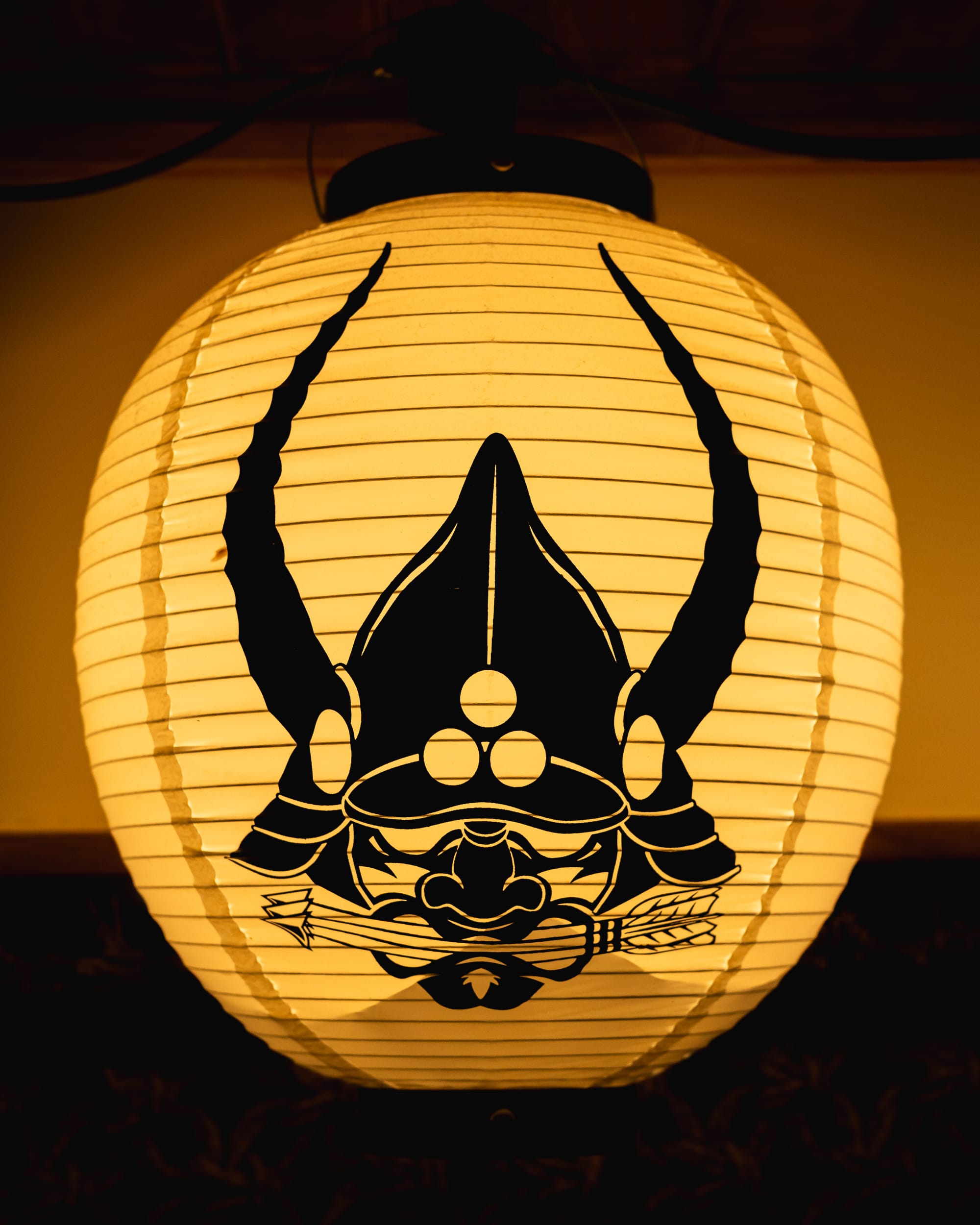 A traditional Japanese lantern with a stylized samurai helmet design, glowing in dim lighting.