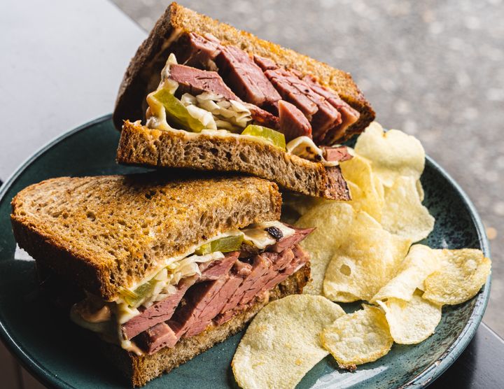 Close up shot of reuben sandwich stacked on-top of each other, with a side of crisps