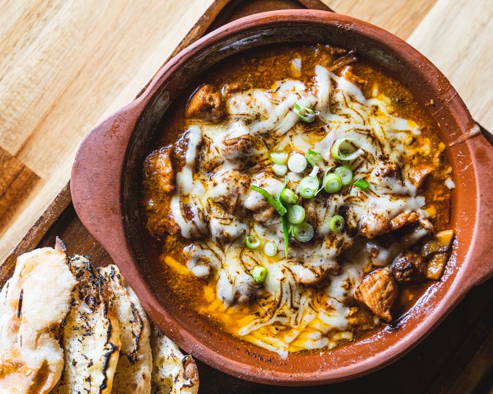 Close up of claypot dish that has cheese ontop of meat, spring onions and a side of turkish bread