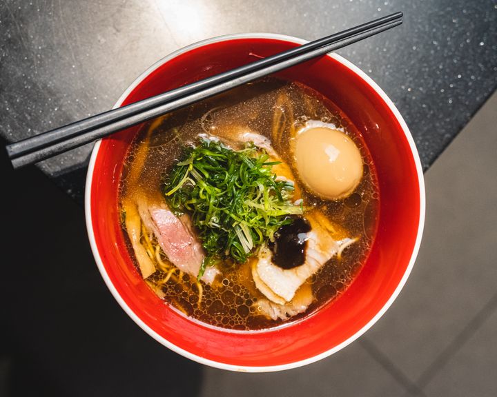 Top down shop of a bowl of soy ramen with egg and a pair of chopsticks rested on-top
