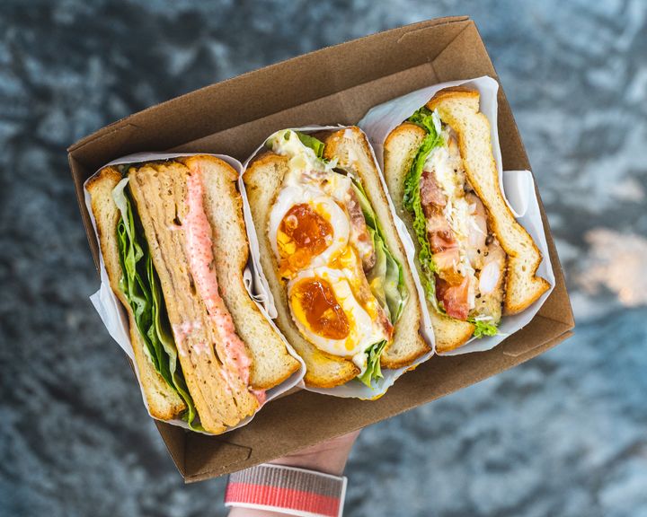 A hand holding a tray of sandwiches which are popping with fillings