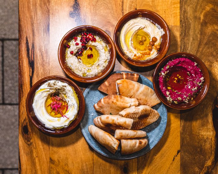 Top down of flat bread surrounded by different bowls of middle eastern dip