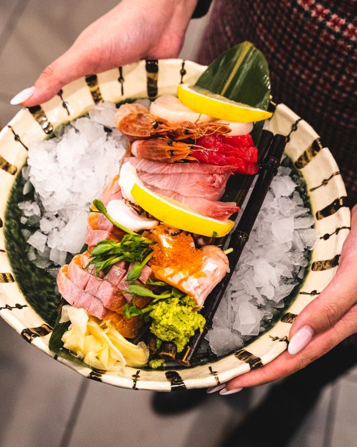 Manicured nails holding a plate of colourful sashimi