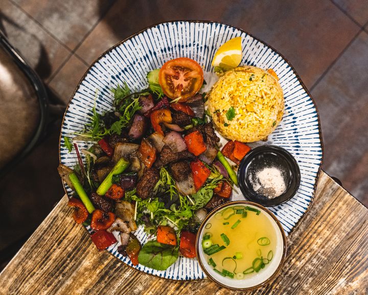 Top down shot of a palte with fried rice, stir fried beef and vegatables, a bowl of soup and a slice of lemon