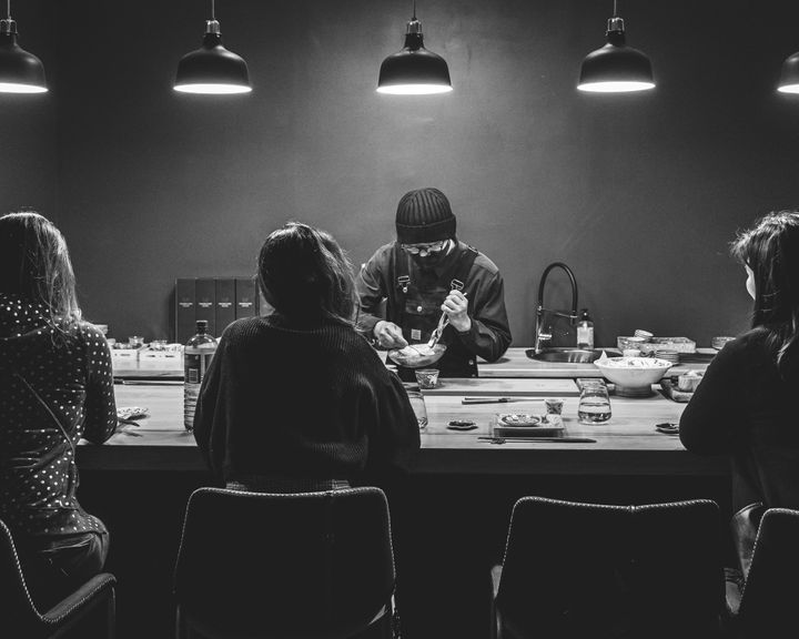 Black and white photo of diners by a counter with a chef cooking infront of them
