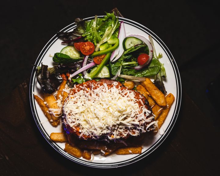 Top down shot of beef parmigiana with shaved cheese, sitting on a bed of chips with a side of salad