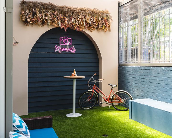 Bike in indoor grassed area with a backdrop which has a neon sign with a camera which says "moments"