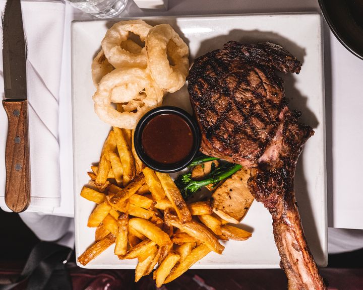 Overhead shot of dry age rib-eye steak with fries, onion rings, mushrooms and greens