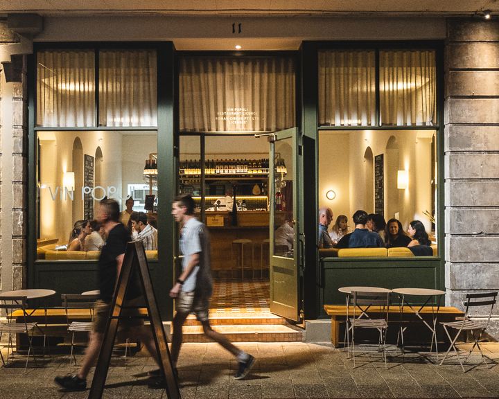 A group of people walking past a restaurant with its' doors open