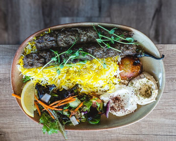 Top down shot of saffron rice, salad, hummuss and two lamb skewers