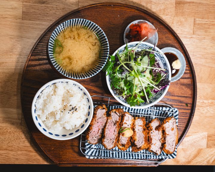 Top down shot of pork katsu, salad, pickled raddish, tonkatsu sauce, miso soup and rice served on a wooden tray