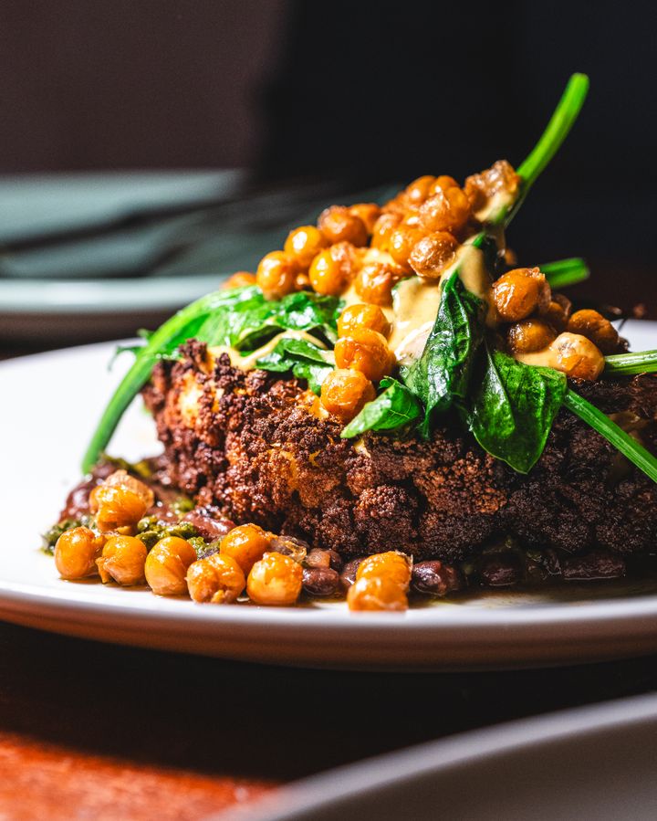 Close of up entire roasted cauliflower head, chickpeas and spinach