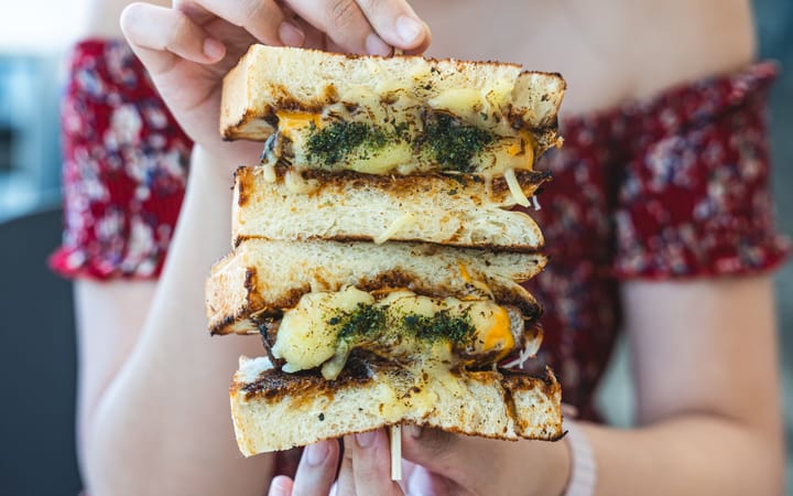 Hand holding a hamburger sandwich with melted cheese and herbs