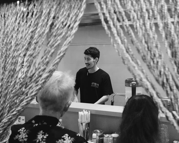 A black and white photo of a smiling waiter interacting with customers in a restaurant.