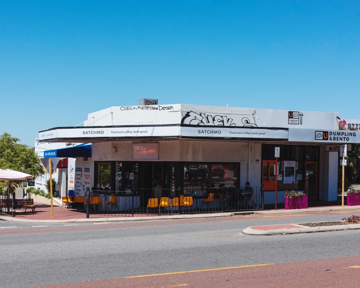 An exterior shot of a café with outdoor seating, a blue sky in the background.