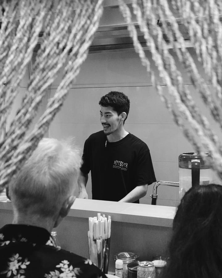 A black and white photo of a smiling waiter interacting with customers in a restaurant.